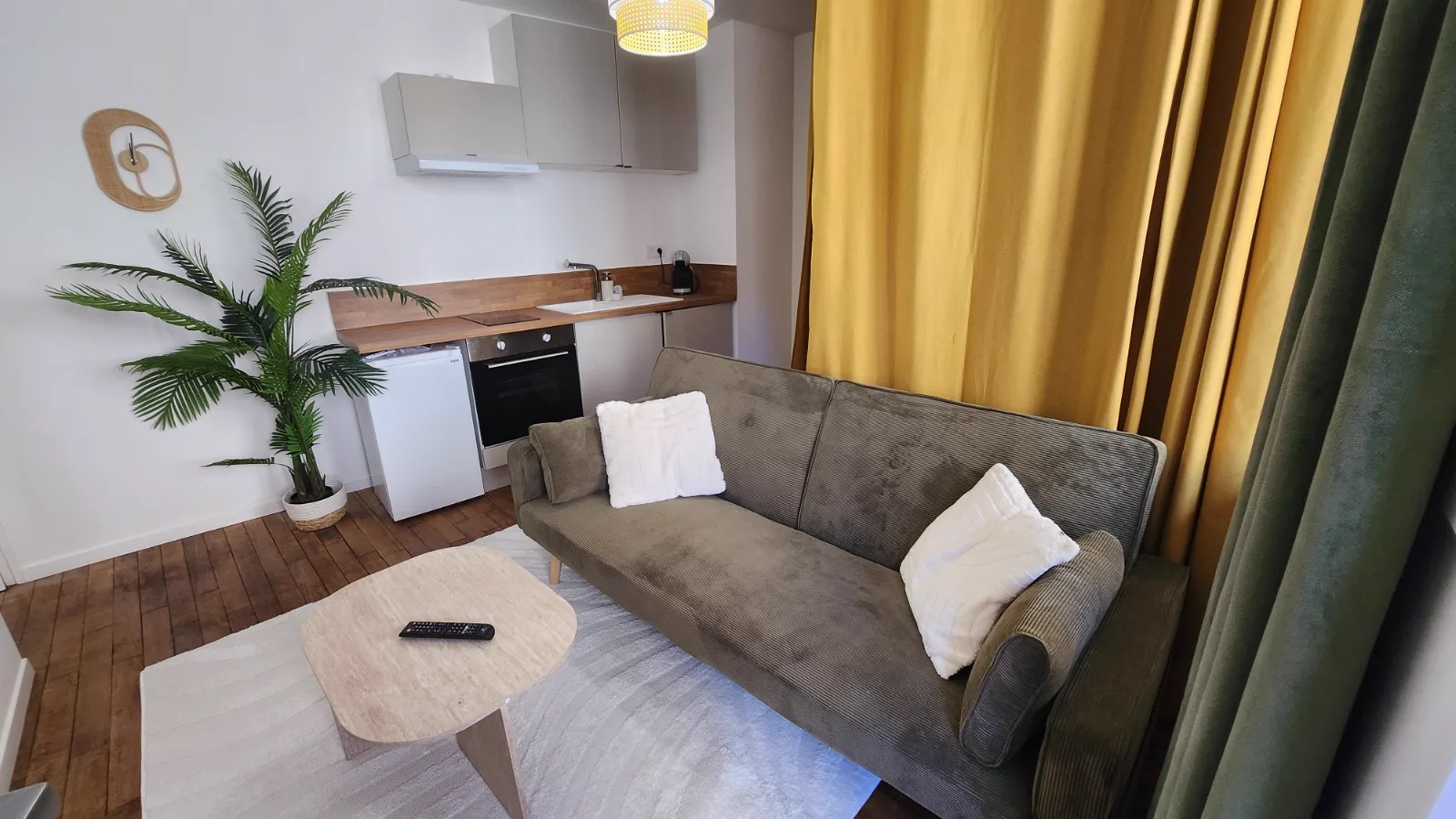 Salon avec canapé, cuisine équipée et rideaux ocre